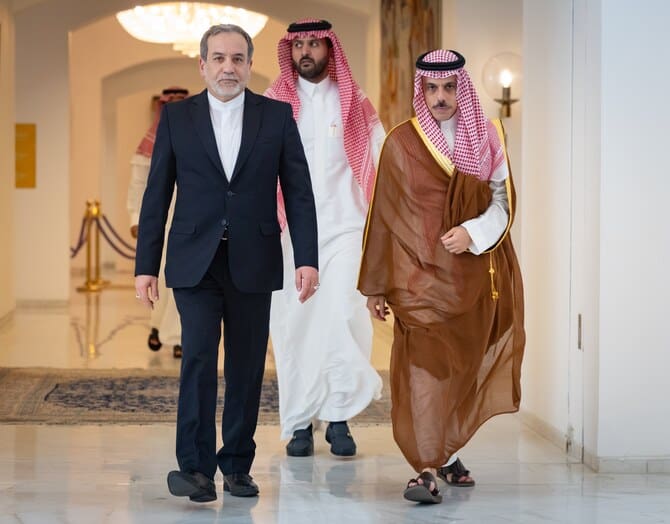 Saudi Foreign Minister Prince Faisal bin Farhan walks alongside Iranian Foreign Minister Abbas Araghchi indoors during an official meeting.