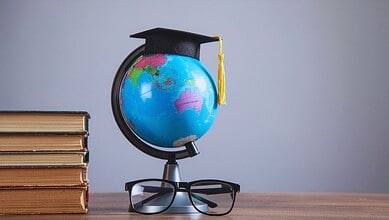 Globe with graduation cap and glasses on a desk, symbolising education and international scholarships.