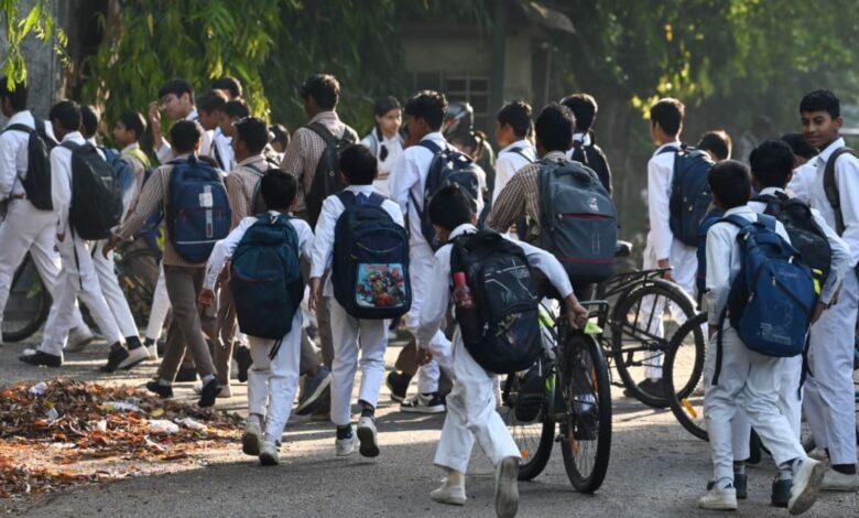 Image shows A group of uniformed Indian school children with backpacks walk and cycle along a tree-lined path.