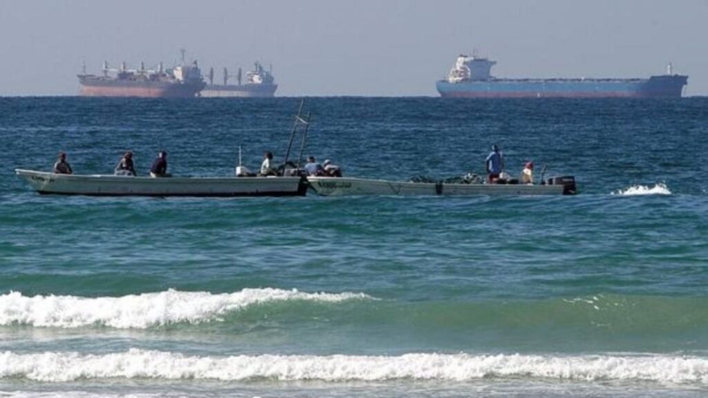 Small fishing boats near the shore with large oil tankers visible in the Strait of Hormuz.