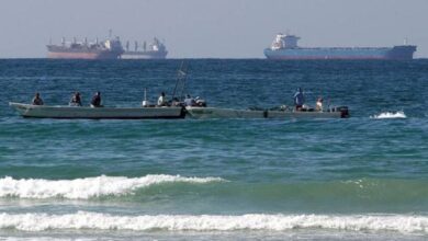 Small fishing boats near the shore with large oil tankers visible in the Strait of Hormuz.
