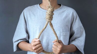 Image shows A person holding a rope noose against their chest.