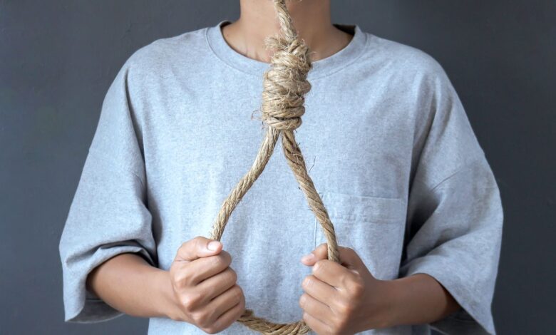 Image shows A person holding a rope noose against their chest.
