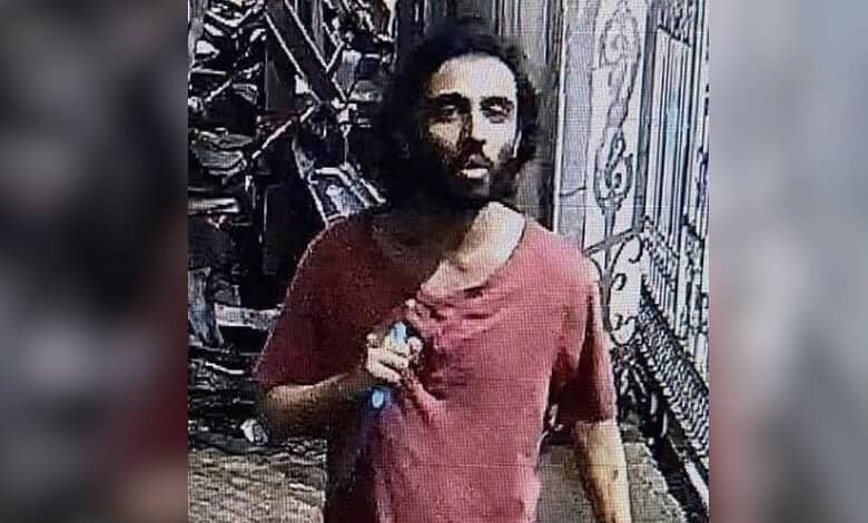 A man with long hair and a beard, dressed in a red shirt, standing outside near a metal fence following an incident involving security guards in Maharashtra.