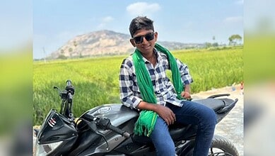 Young boy sitting on a motorcycle in a rural area, with green fields and hills in the background, after a.
