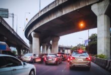 Image shows Cars stuck in heavy traffic under a multi-level concrete highway interchange at dusk.