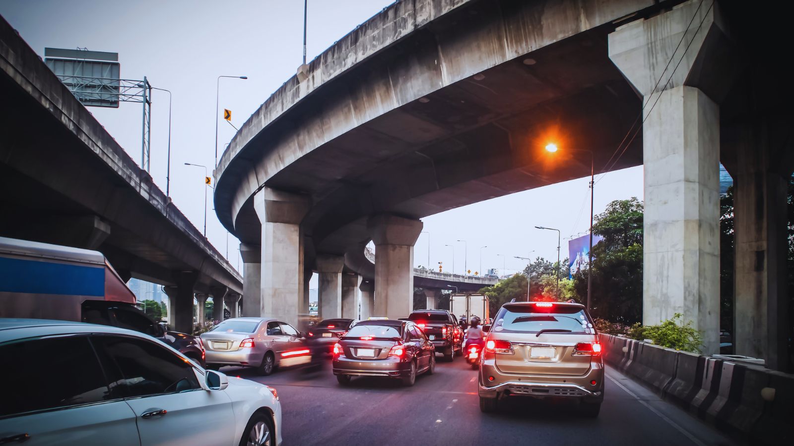 Image shows Cars stuck in heavy traffic under a multi-level concrete highway interchange at dusk.