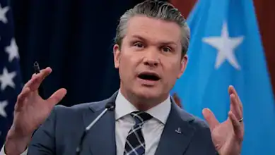 US Defence Secretary Pete Hegseth speaks during a press briefing with US and Somali flags in the background.