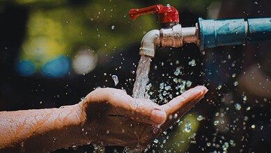 A close-up of a hand under a running tap, highlighting the importance of reporting water wastage in Hyderabad to conserve water resources.
