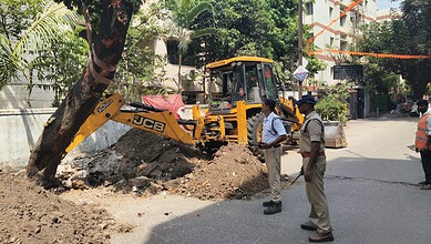 Excavation work on a city street with police officers inspecting the site and a JCB backhoe loader in the.