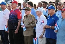 Cuban citizens and officials gather holding small Cuban flags during a public event.