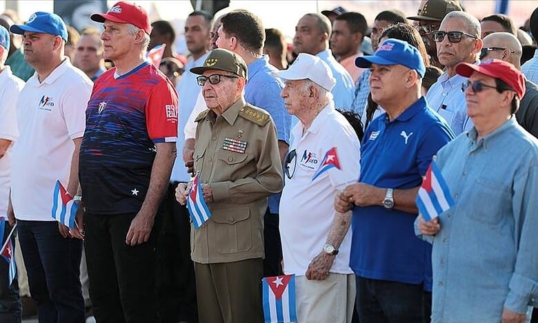 Cuban citizens and officials gather holding small Cuban flags during a public event.