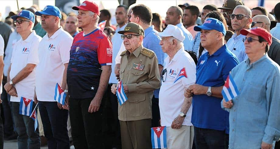 Cuban citizens and officials gather holding small Cuban flags during a public event.