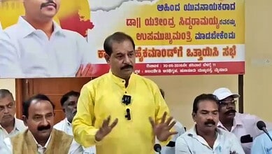 Political leader speaking at a rally with supporters and a banner in the background.