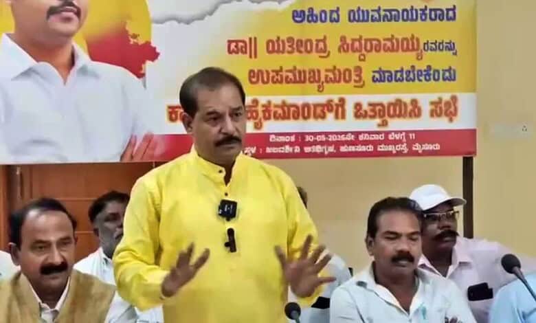 Political leader speaking at a rally with supporters and a banner in the background.