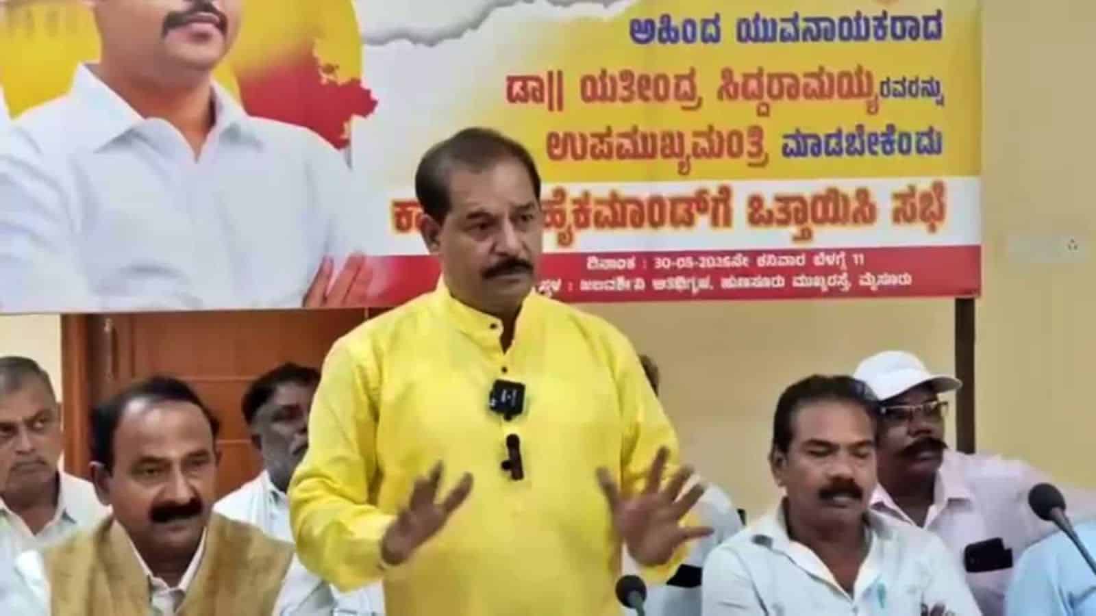 Political leader speaking at a rally with supporters and a banner in the background.