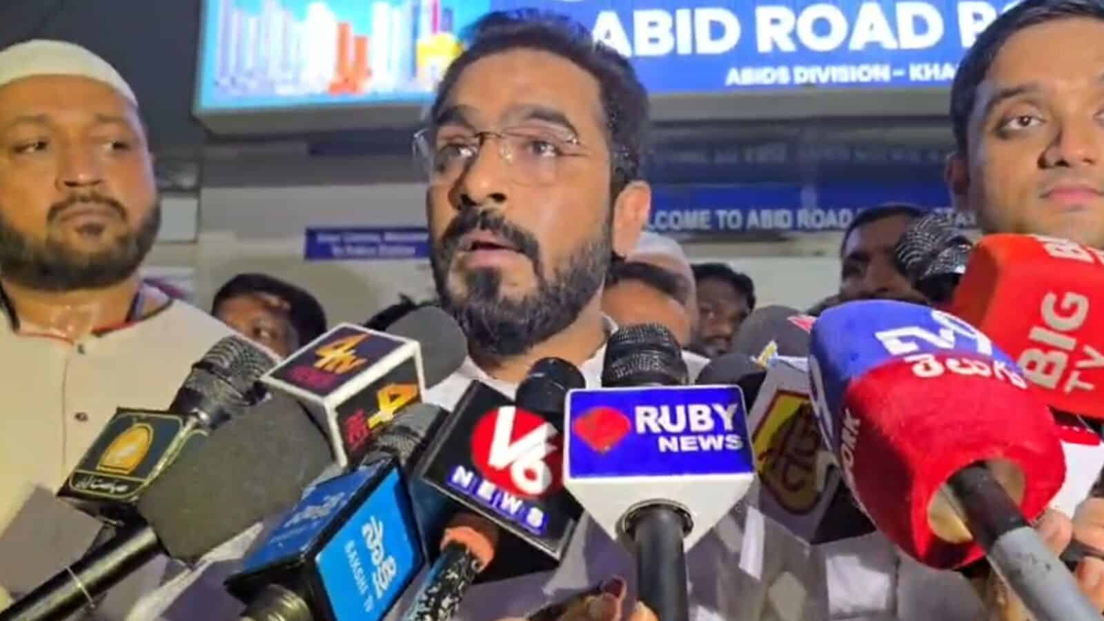 Man speaking at a press conference surrounded by microphones from various news outlets.