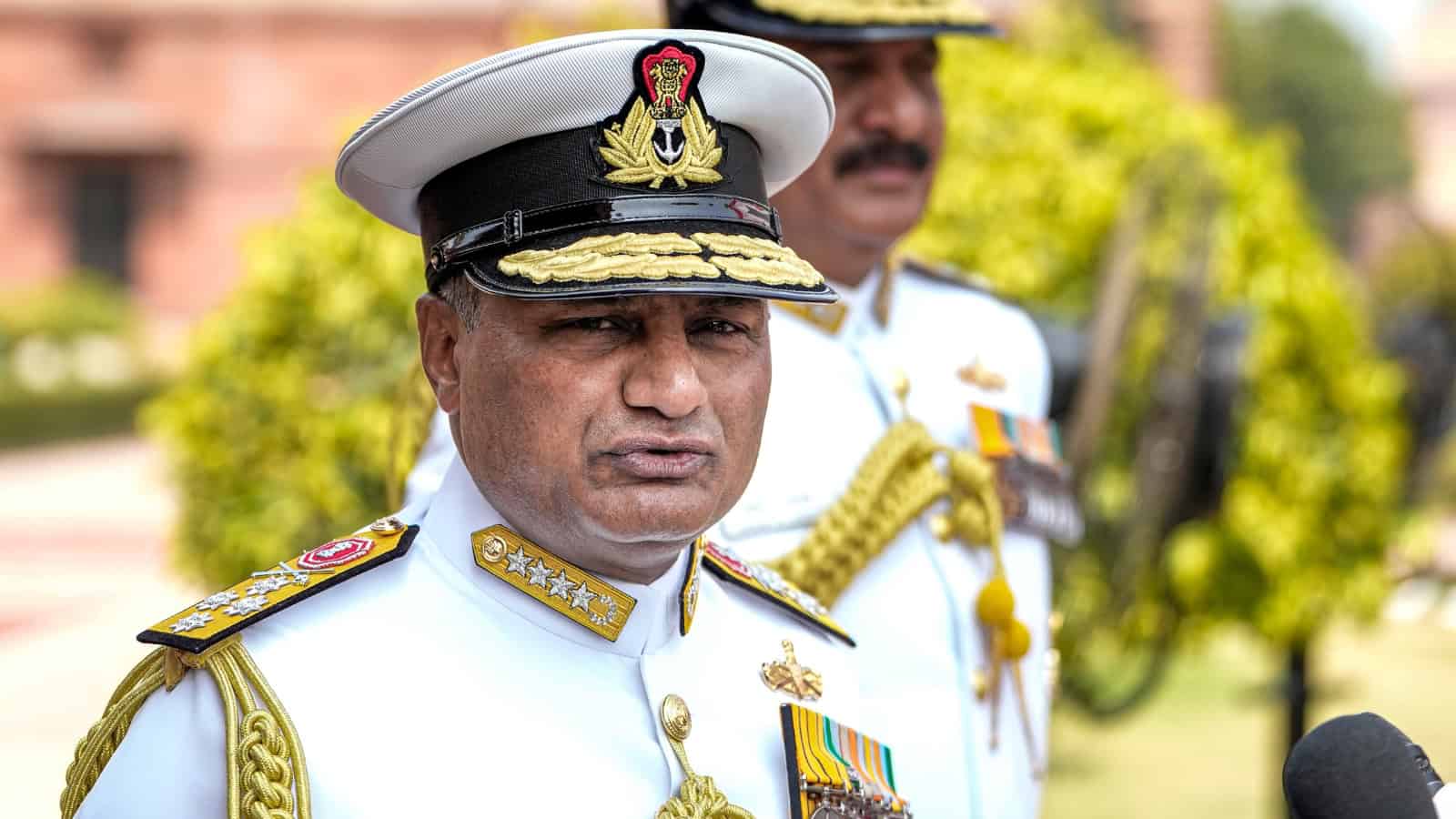 Indian naval officer in uniform during a formal event with greenery in the background.