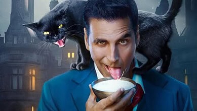 A man in a blue suit with a black cat on his shoulder, licking a bowl of milk, in a dark, cityscape backg.