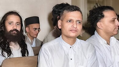 A man in white traditional attire attending a formal event with other individuals in the background.