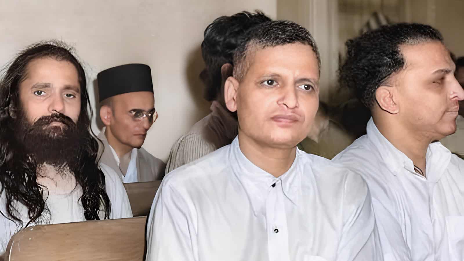 A man in white traditional attire attending a formal event with other individuals in the background.