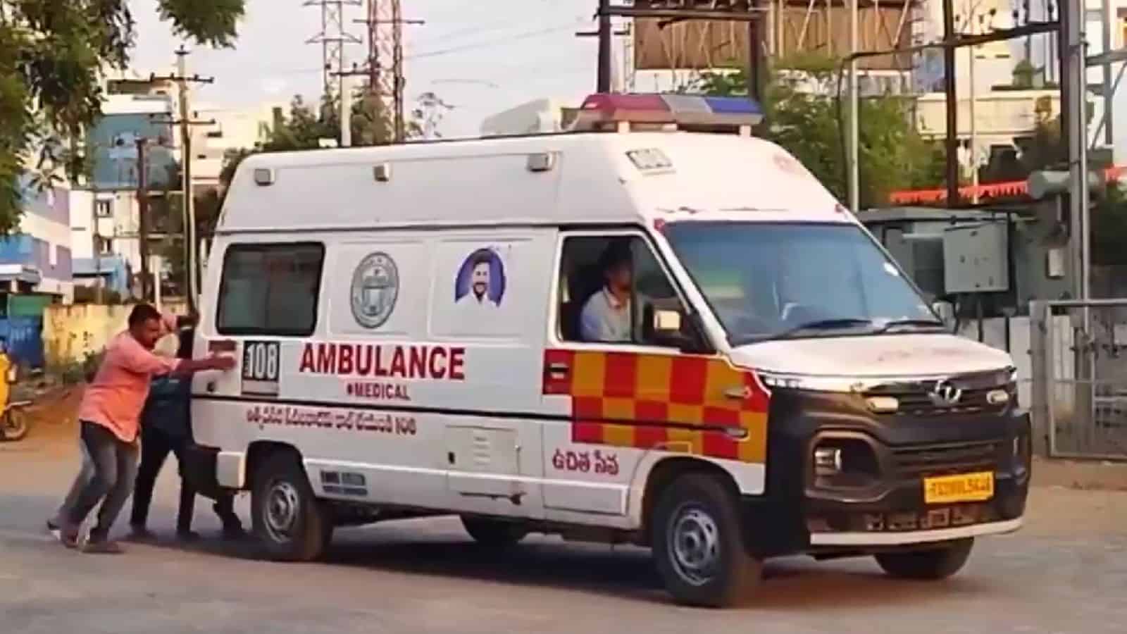 An ambulance being pushed by two people on a city street in India.