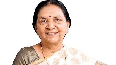 A woman smiling, wearing traditional Indian attire and jewelry, with a bindi on her forehead.