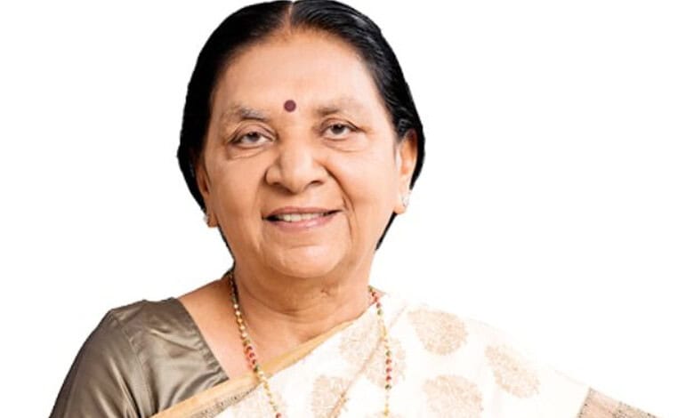 A woman smiling, wearing traditional Indian attire and jewelry, with a bindi on her forehead.