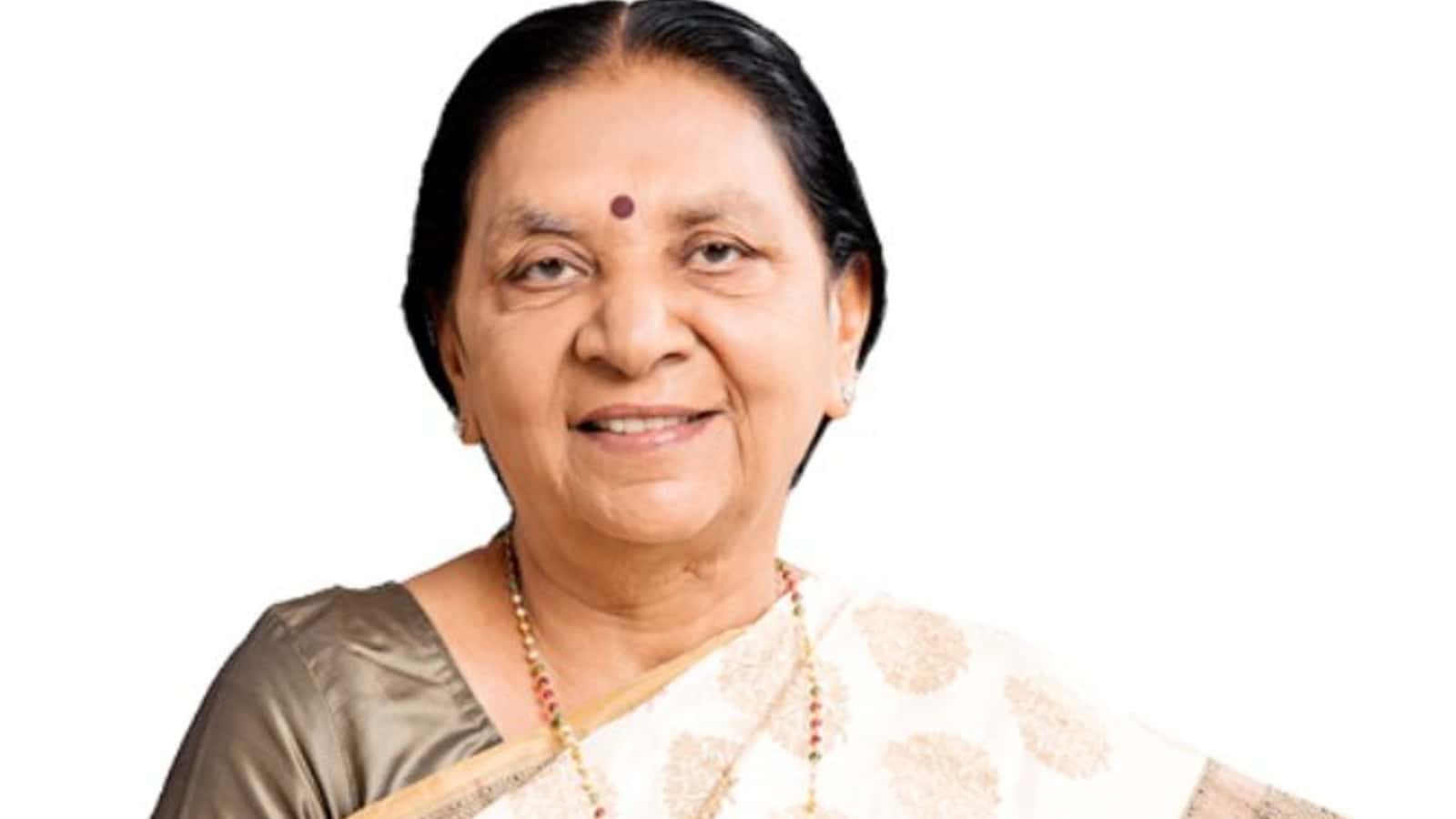 A woman smiling, wearing traditional Indian attire and jewelry, with a bindi on her forehead.