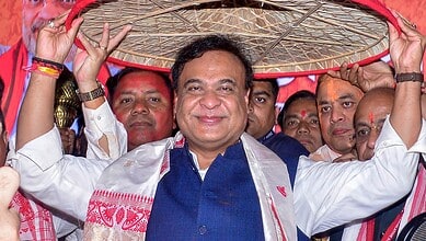 An image of a smiling political leader holding a traditional umbrella during a celebration in Assam.