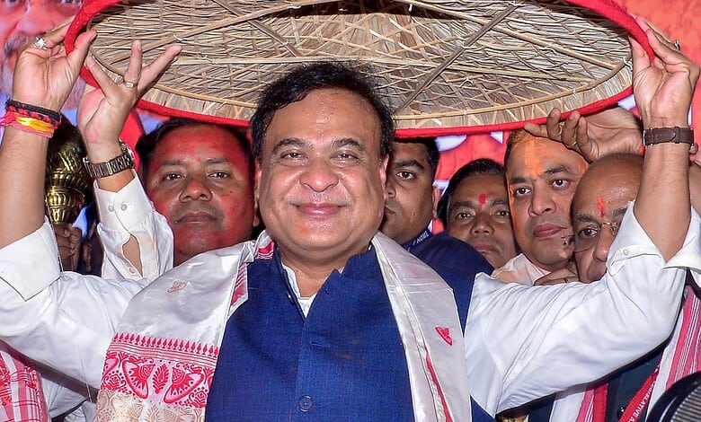 An image of a smiling political leader holding a traditional umbrella during a celebration in Assam.