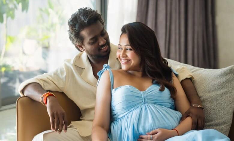 Happy couple sitting on sofa, smiling, with pregnant woman in blue dress, celebrating pregnancy indoors.