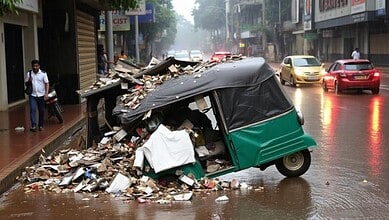 Flooded street with a damaged auto rickshaw and debris after heavy rain, causing disruption in urban traf.