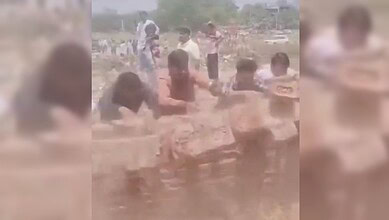 A woman and children playing in muddy water outdoors on a sunny day, with a rural background.