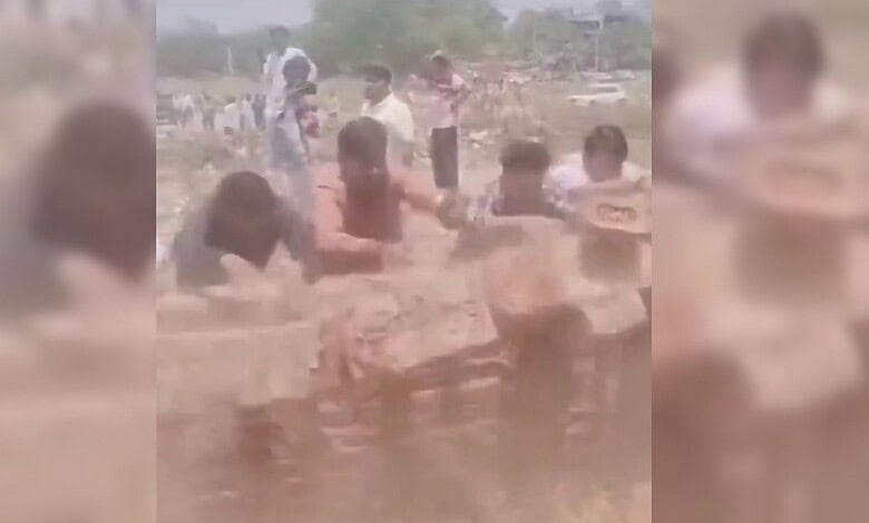 A woman and children playing in muddy water outdoors on a sunny day, with a rural background.