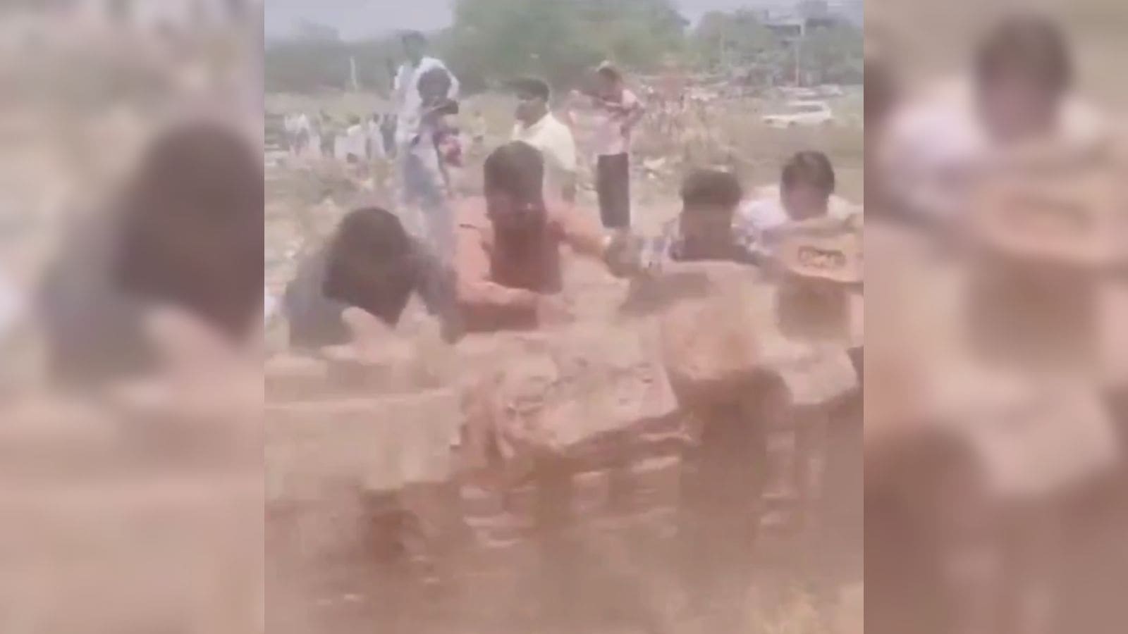 A woman and children playing in muddy water outdoors on a sunny day, with a rural background.