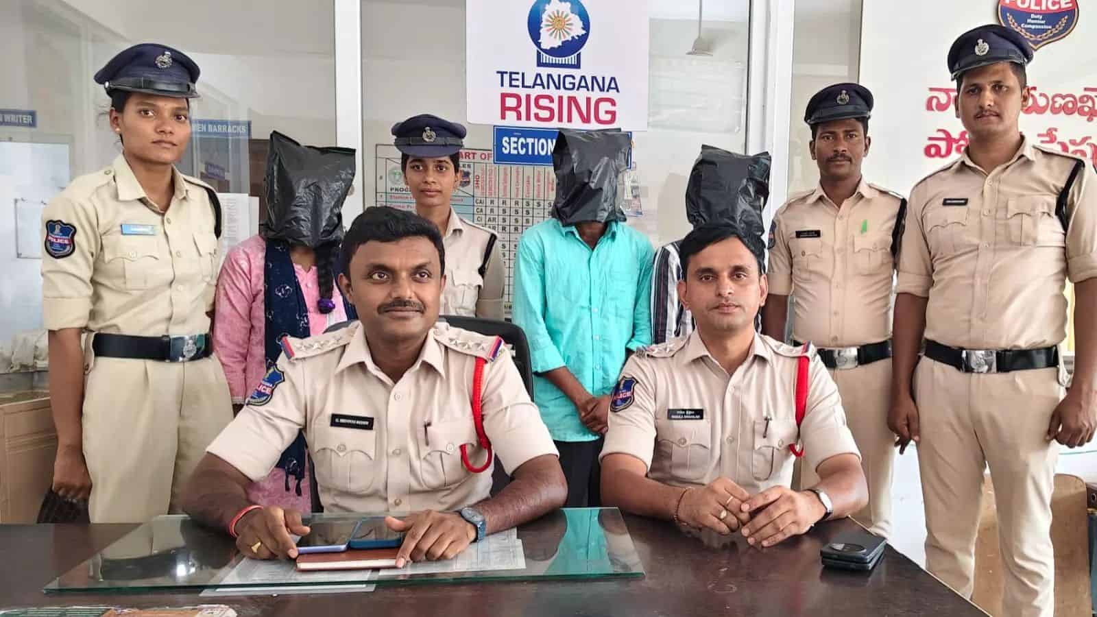 Police officers with two individuals wearing black bags over their heads at Telangana Rising event.