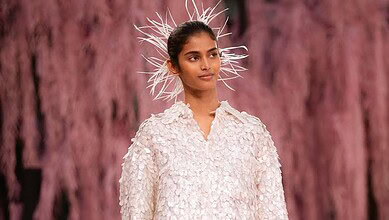 A young female model wearing a textured white dress and a striking feathered headpiece, showcasing avant-.