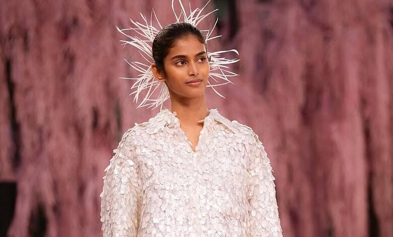 A young female model wearing a textured white dress and a striking feathered headpiece, showcasing avant-.