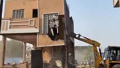 A construction worker operating a JCB excavator demolishing a building in an urban area.