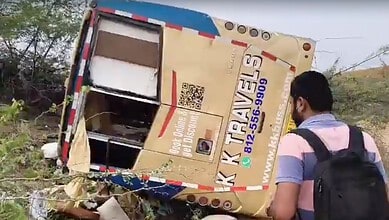 A bus accident with a tilted bus on the roadside, person observing the scene, likely in India.