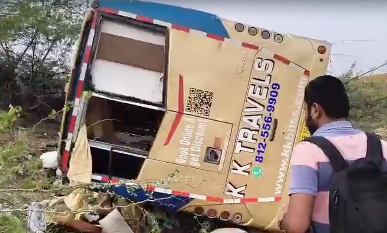 A bus accident with a tilted bus on the roadside, person observing the scene, likely in India.