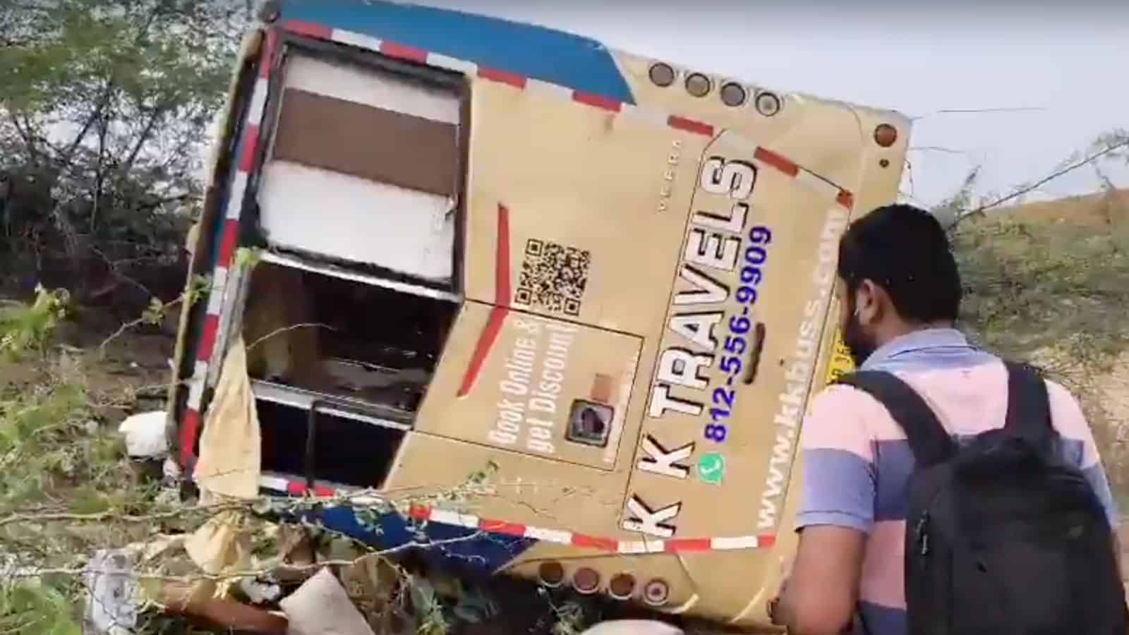 A bus accident with a tilted bus on the roadside, person observing the scene, likely in India.