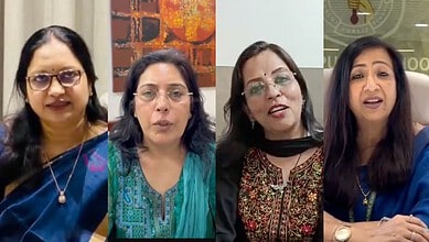 A woman speaking at a press conference with three other women, all dressed in traditional Indian attire,.