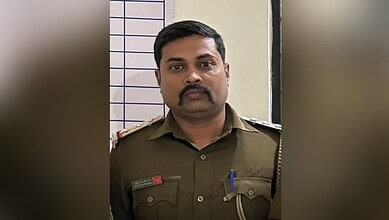 Police officer in uniform with badges and pens, standing indoors against a tiled wall.