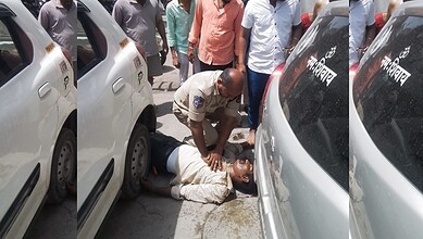 A woman lying on the ground between parked cars, receiving assistance from a police officer in a crowded.