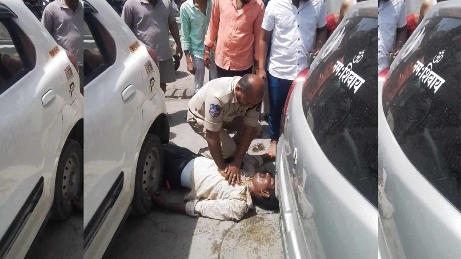 A woman lying on the ground between parked cars, receiving assistance from a police officer in a crowded.