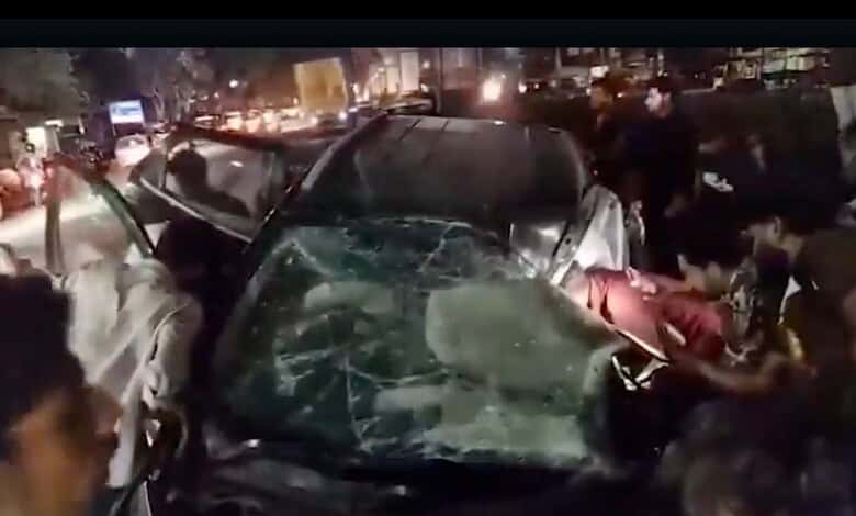 Car crash at night with multiple damaged vehicles and emergency responders on busy city street.