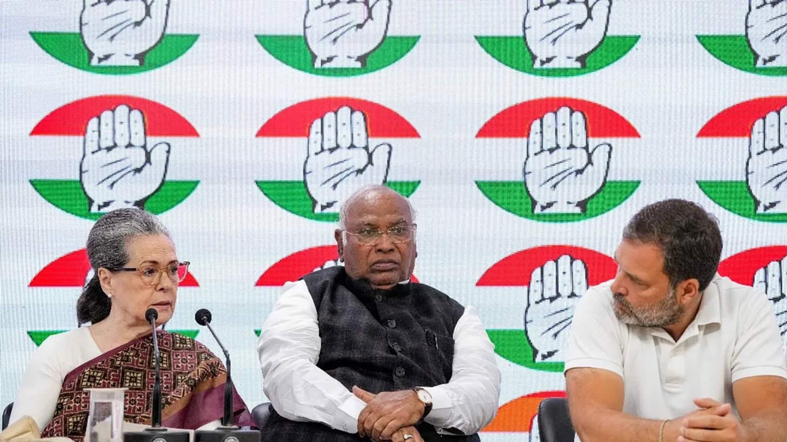 Indian political leaders at a press conference with the Congress party symbol in the background.