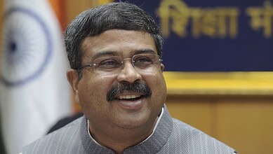 Indian politician smiling at a public event with the Indian flag in the background.